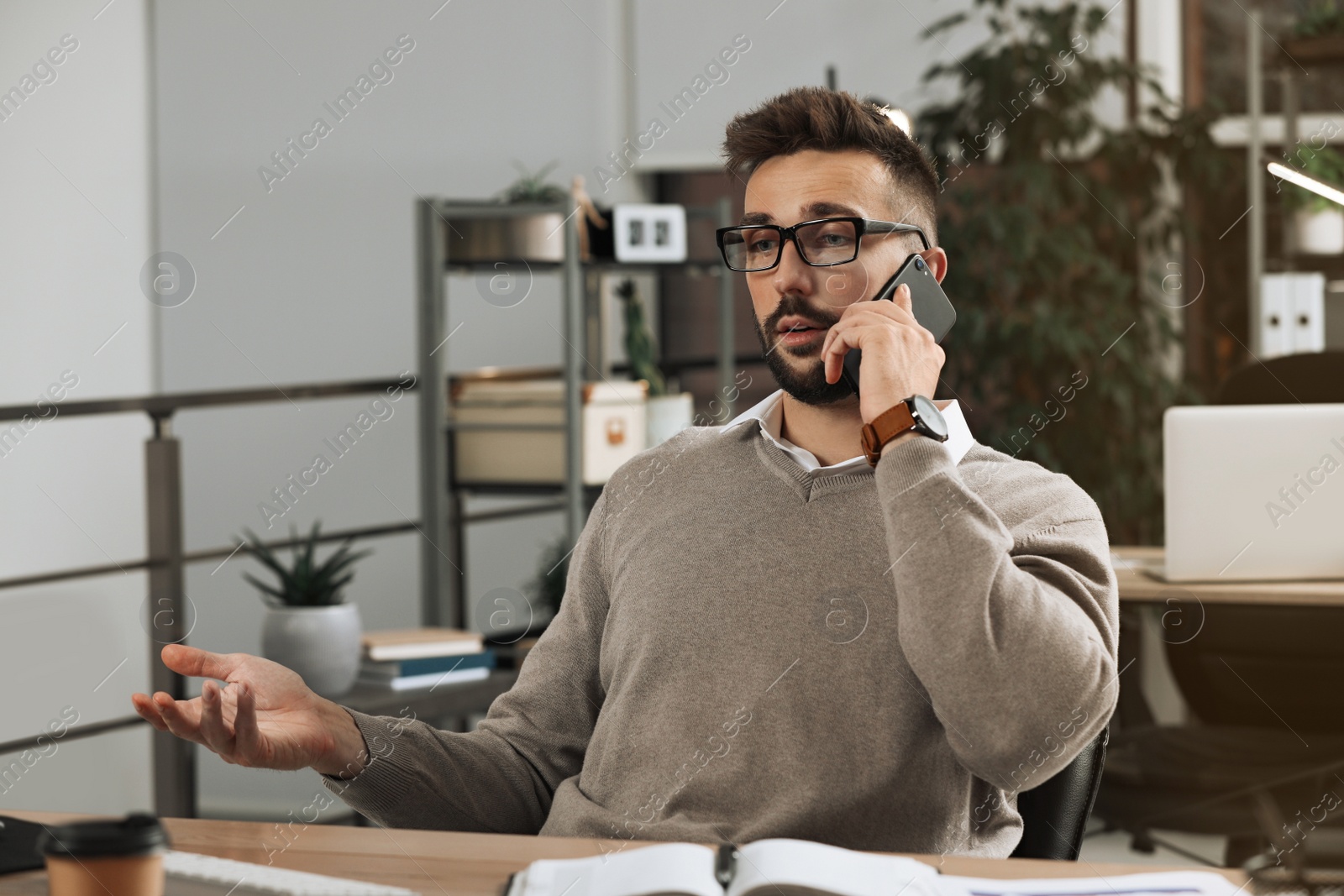 Photo of Man talking on phone while working at table in office