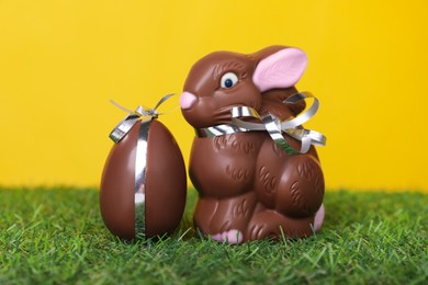 Photo of Easter celebration. Cute chocolate bunny and egg on grass against yellow background