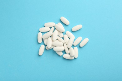 Photo of Pile of vitamin pills on light blue background, flat lay