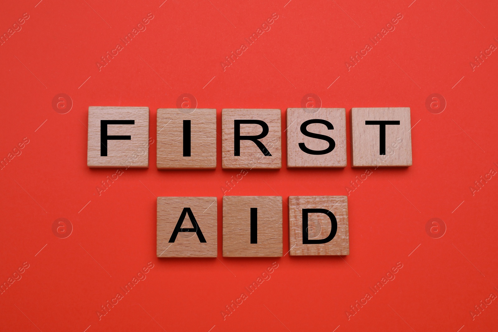 Photo of Words First Aid made of wooden cubes on coral background, flat lay