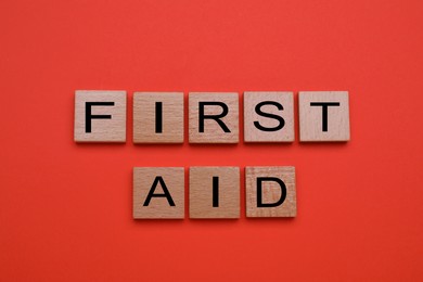 Words First Aid made of wooden cubes on coral background, flat lay
