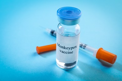 Monkeypox vaccine in glass vial and syringe on light blue background, space for text