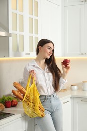 Photo of Woman with string bag of baguettes and apple in kitchen