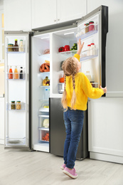 Little girl near open refrigerator in kitchen