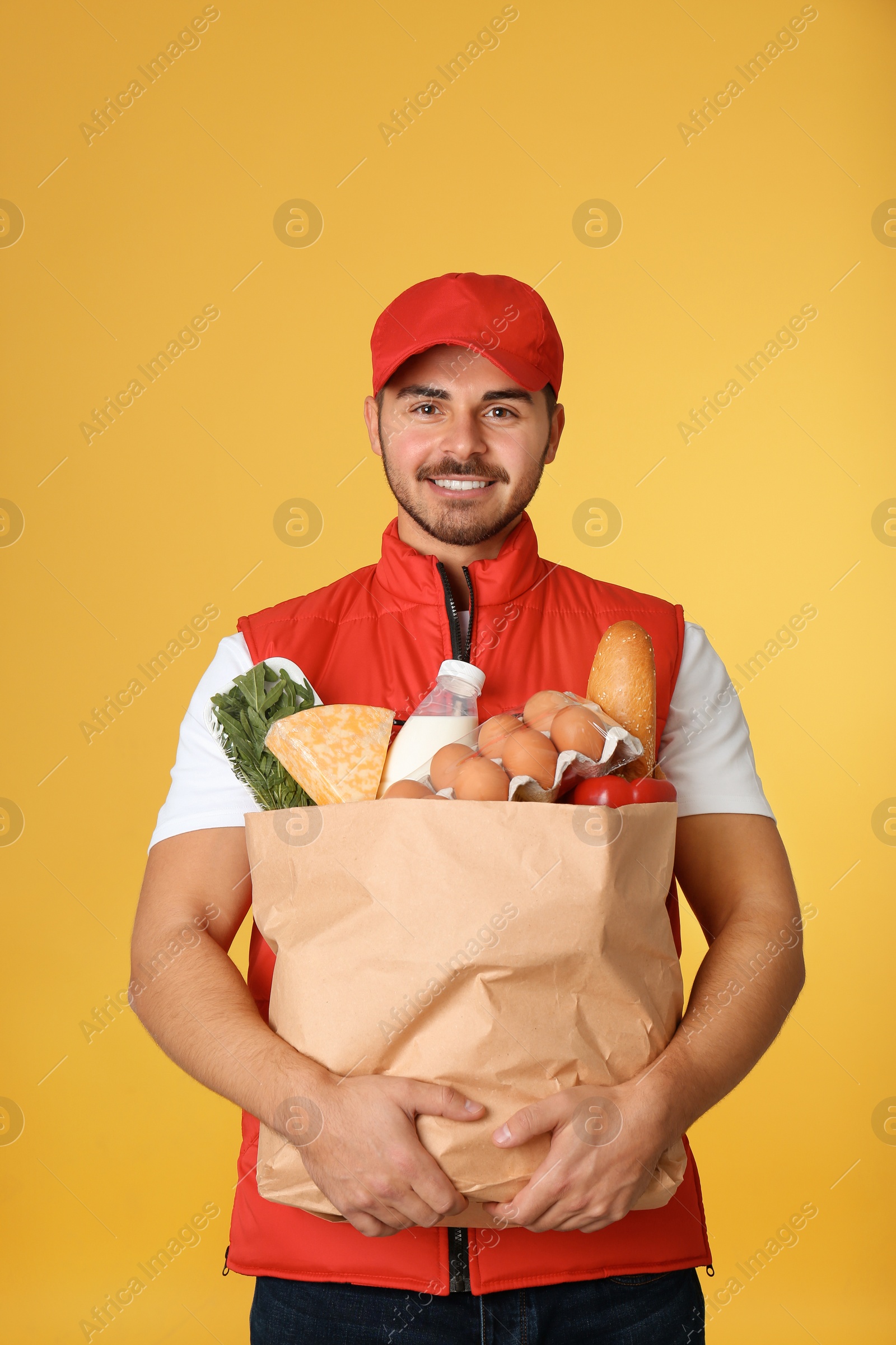 Photo of Young man holding paper bag with products on color background. Food delivery service