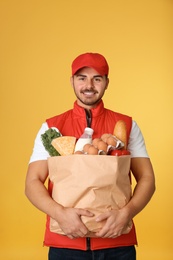 Young man holding paper bag with products on color background. Food delivery service