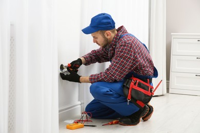 Photo of Electrician with pliers repairing power socket in room