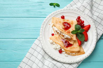 Photo of Delicious thin pancakes with cottage cheese, jam and berries on light blue wooden table, flat lay