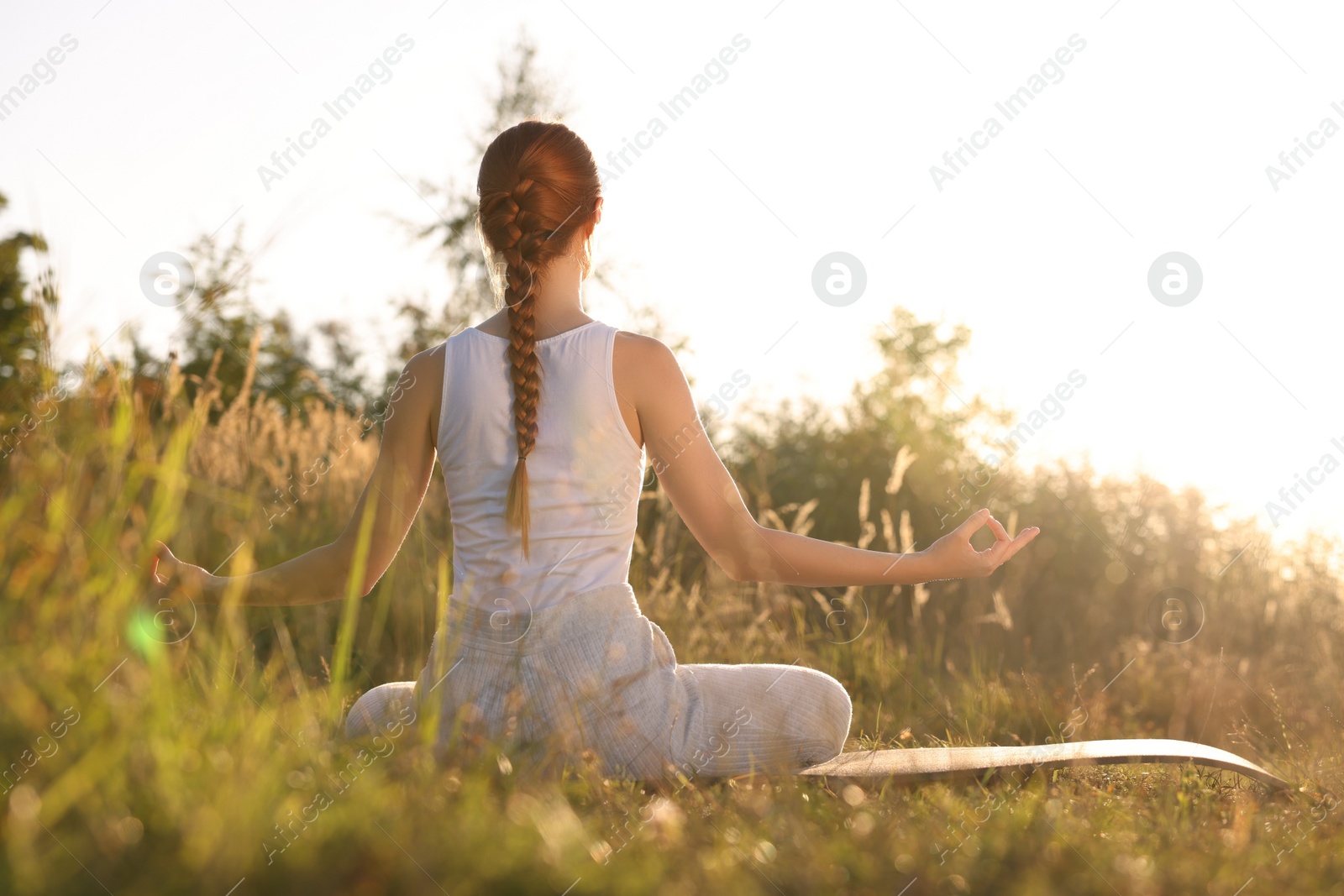 Photo of Woman practicing Padmasana on yoga mat outdoors on sunny day, back view. Lotus pose