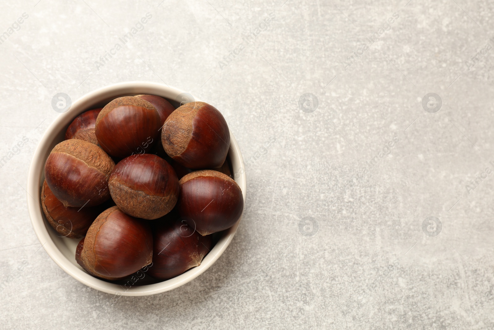 Photo of Roasted edible sweet chestnuts in bowl on light grey table, top view. Space for text