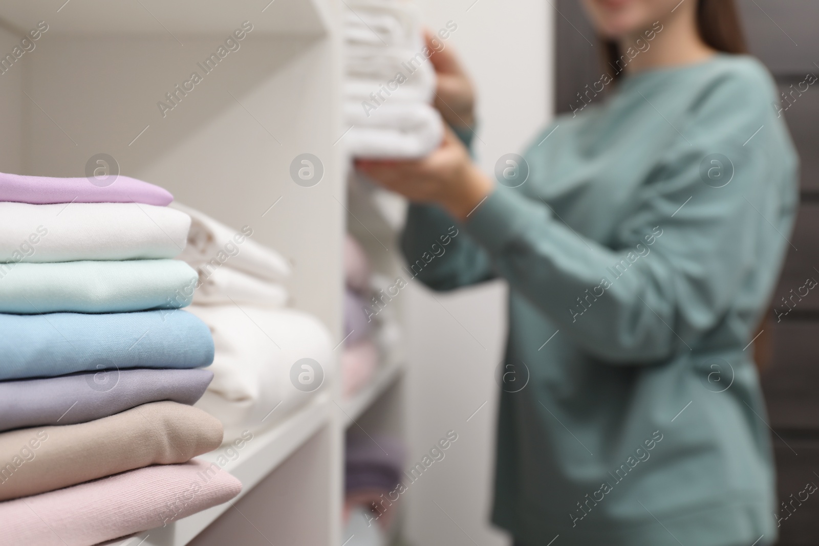 Photo of Stack of bed linens on shelf in shop. Customer choosing towels indoors, selective focus