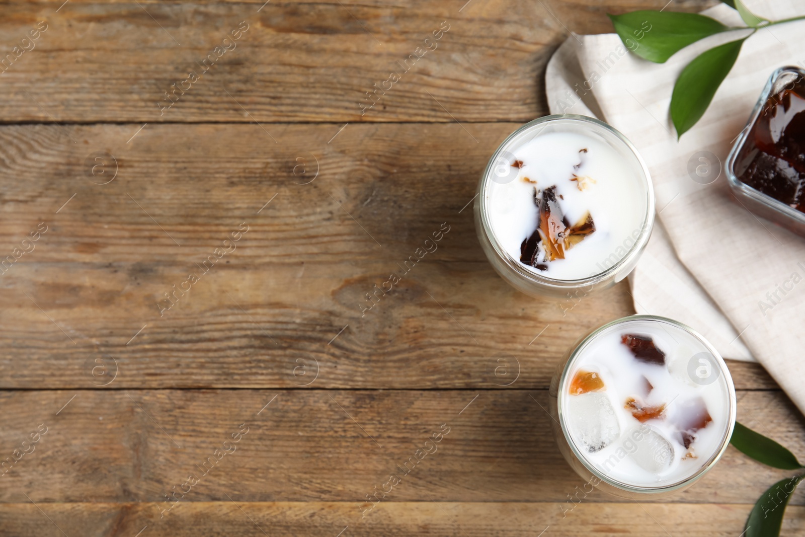 Photo of Glasses of milk with delicious grass jelly on wooden table, flat lay. Space for text