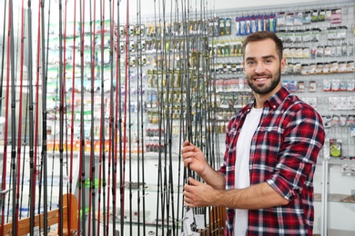 Photo of Man choosing fishing rod in sports shop. Space for text
