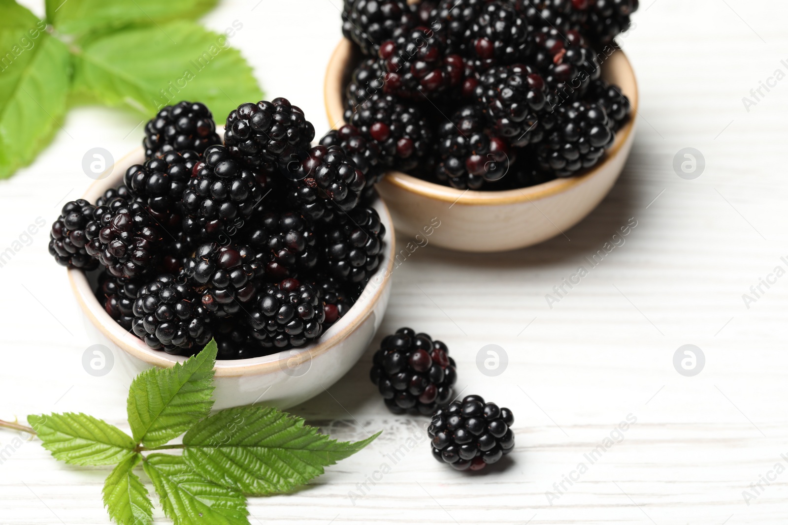 Photo of Ripe blackberries and green leaves on white wooden table, closeup