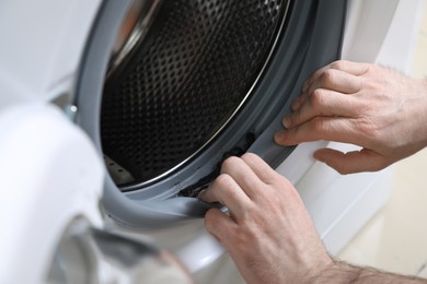 Photo of Man cleaning dirty seals of washing machine, closeup