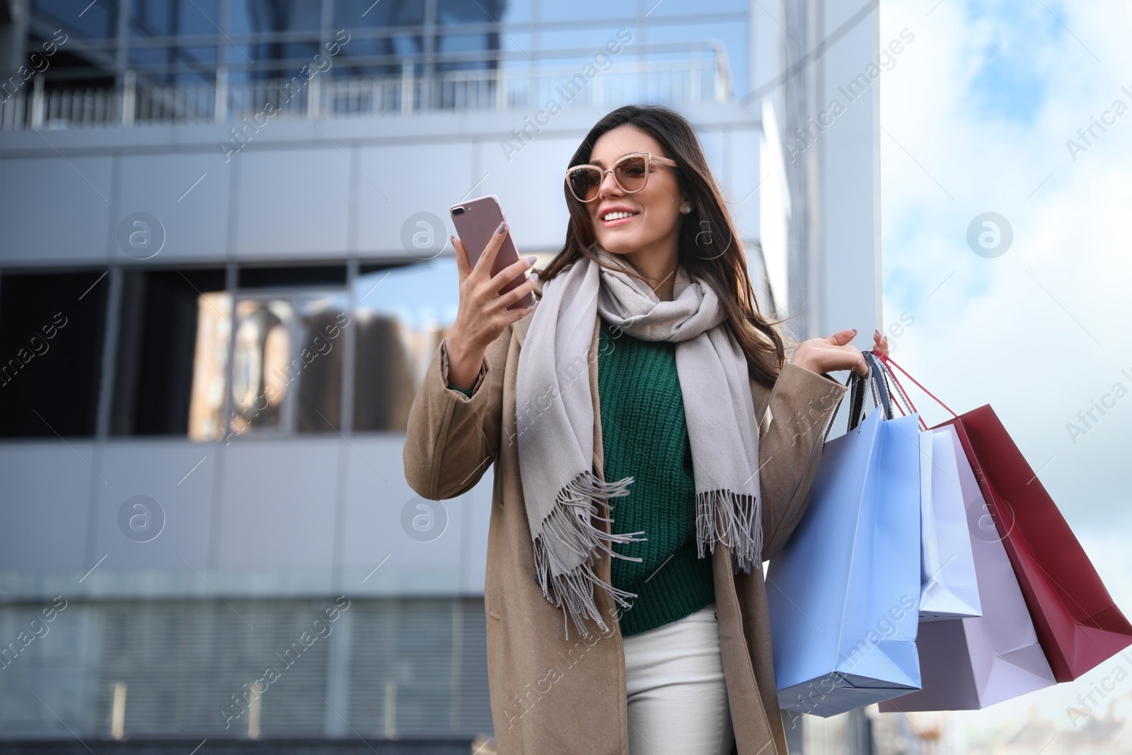 Photo of Beautiful young woman with shopping bags and smartphone outdoors