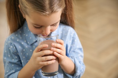 Photo of Cute little child drinking tasty chocolate milk indoors, closeup