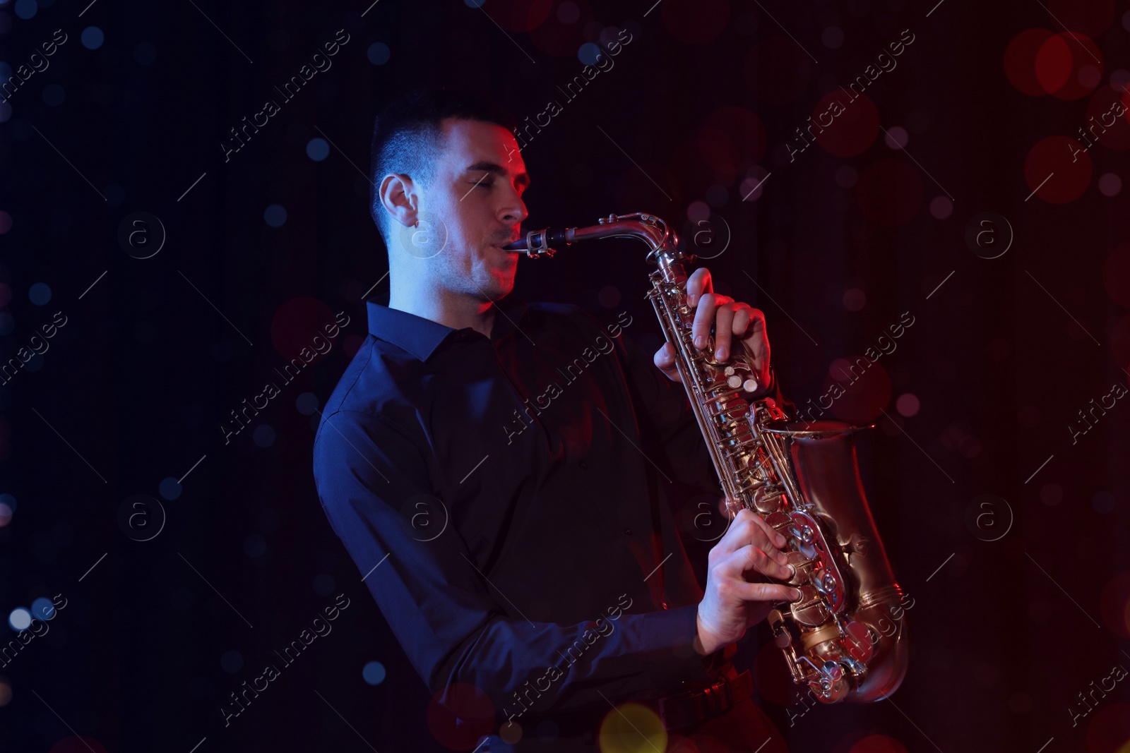 Image of Young man playing saxophone on dark background. Bokeh effect