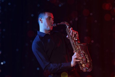 Image of Young man playing saxophone on dark background. Bokeh effect