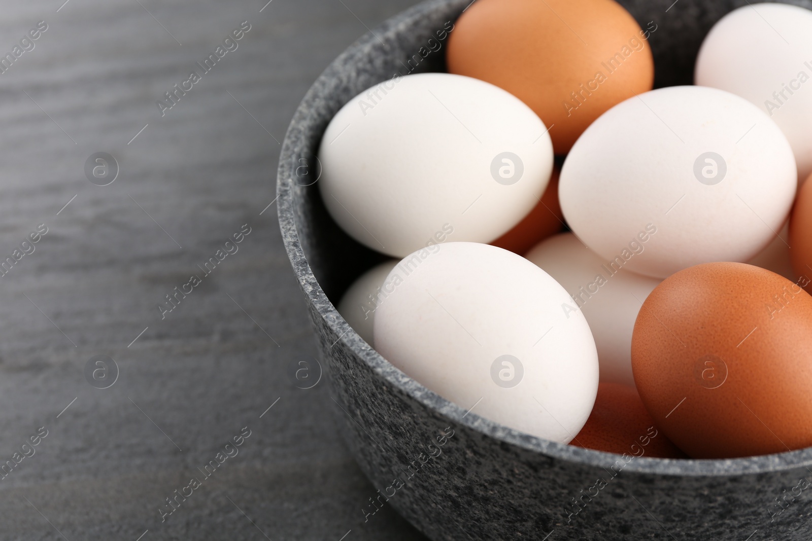 Photo of Unpeeled boiled eggs in saucepan on dark grey table, closeup. Space for text