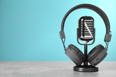 Photo of Microphone and modern headphones on grey table against light blue background, space for text
