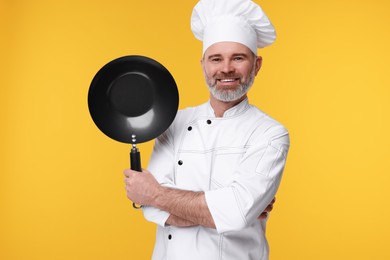 Photo of Happy chef in uniform with wok on orange background