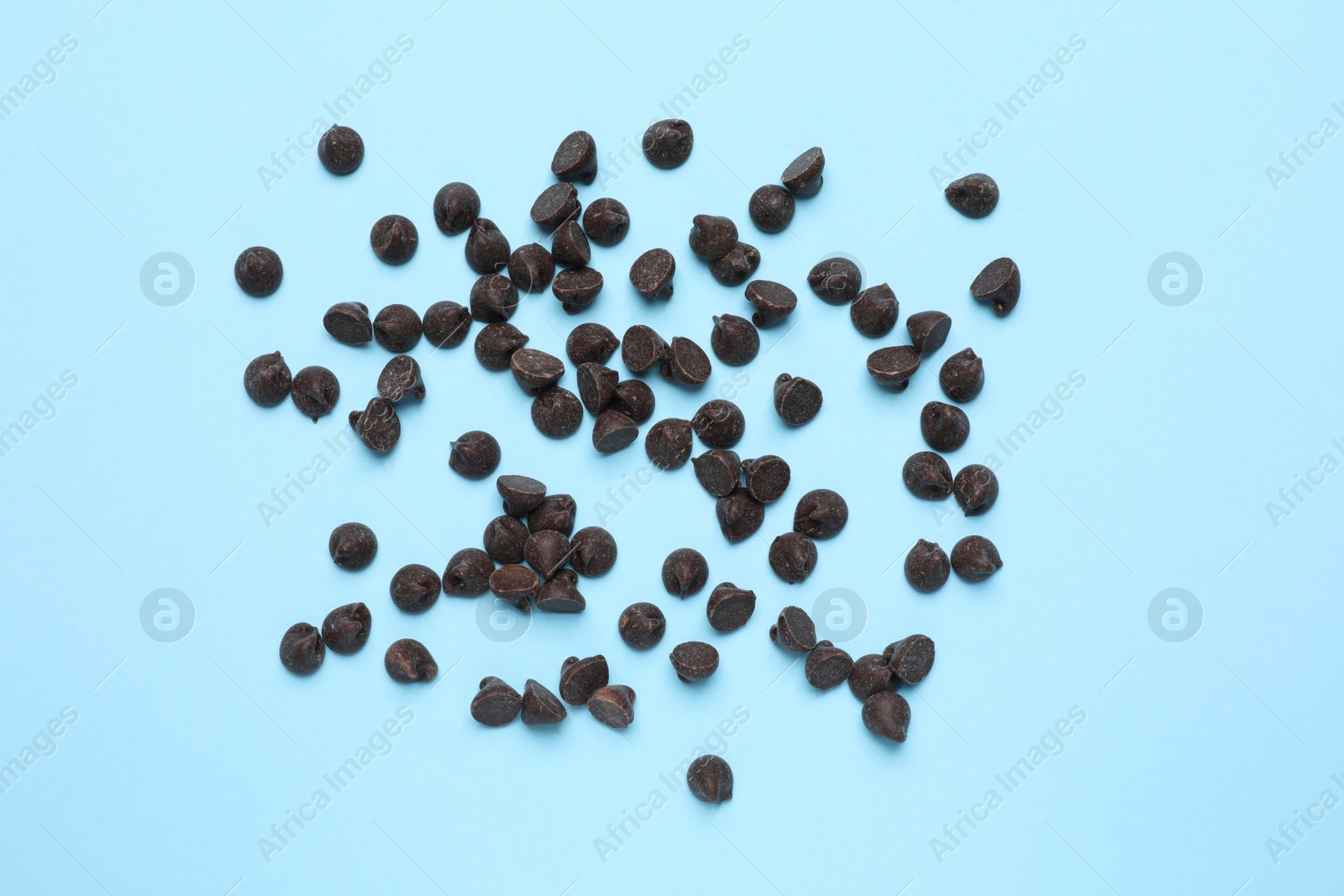 Photo of Delicious dark chocolate chips on light blue background, top view