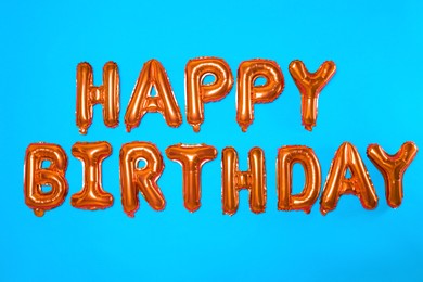 Phrase HAPPY BIRTHDAY made of orange foil balloon letters on light blue background
