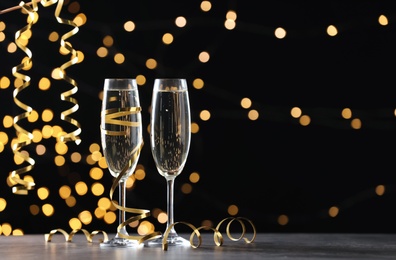 Glasses of champagne and serpentine streamers against black background with blurred lights. Space for text