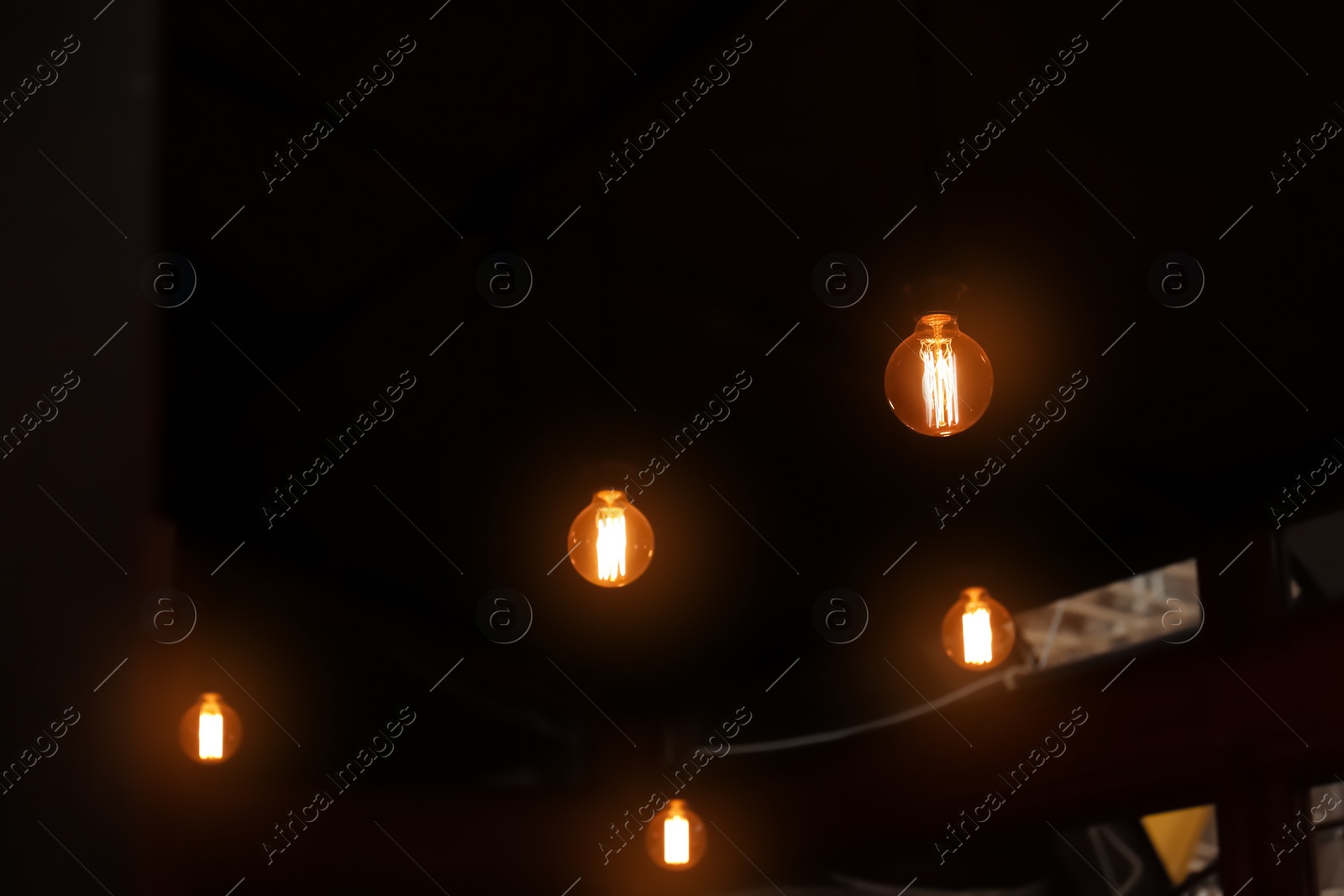 Photo of Glowing lamp bulbs in dark room. Space for text