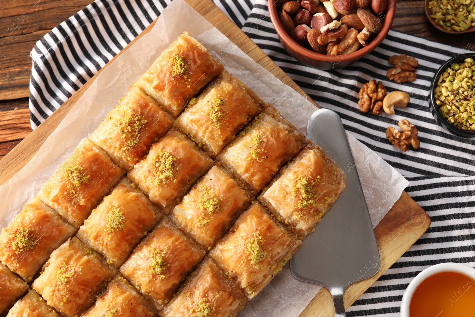 Photo of Delicious sweet baklava with ingredients and cake server on table, flat lay