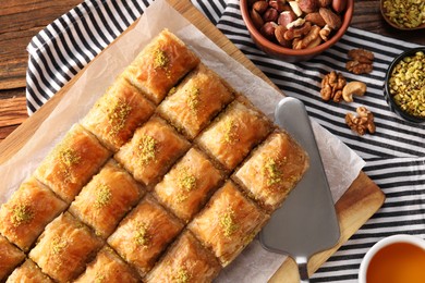 Photo of Delicious sweet baklava with ingredients and cake server on table, flat lay
