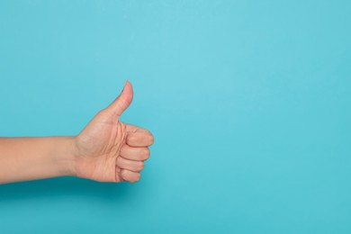 Photo of Woman showing thumb up on light blue background, closeup. Space for text