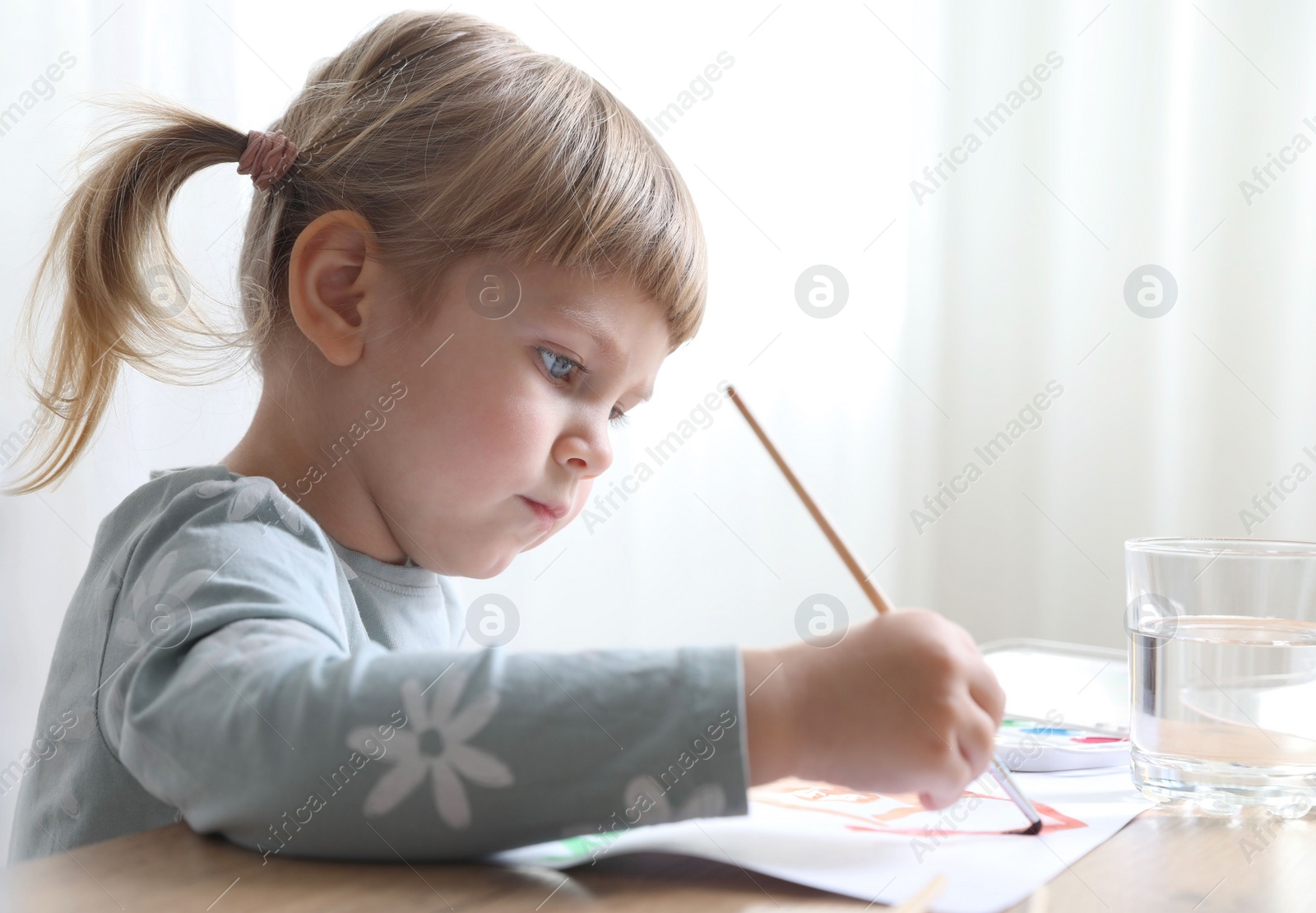 Photo of Cute little girl drawing with brush at wooden table indoors. Child`s art