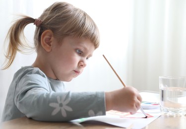 Cute little girl drawing with brush at wooden table indoors. Child`s art