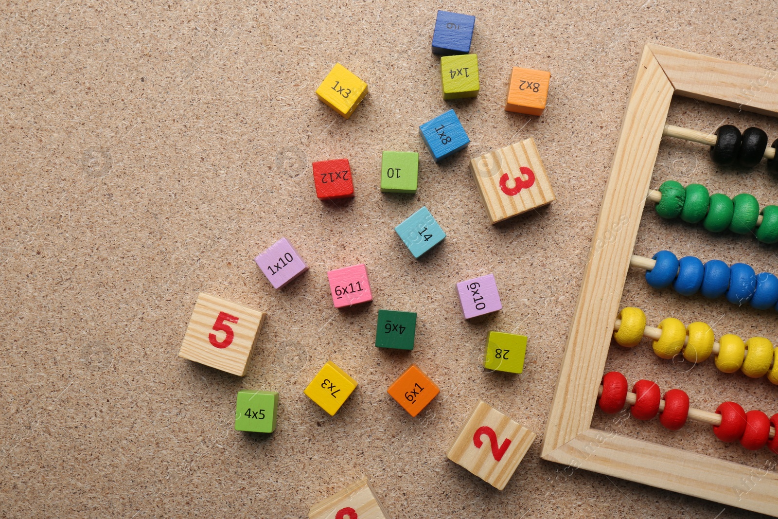 Photo of Wooden cubes with numbers and multiplications near abacus on fiberboard, flat lay. Space for text