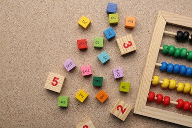 Photo of Wooden cubes with numbers and multiplications near abacus on fiberboard, flat lay. Space for text
