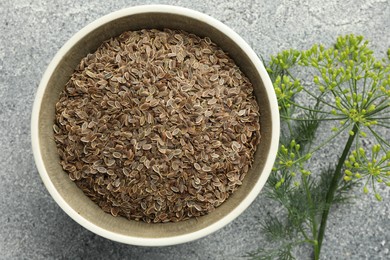 Photo of Bowl of dry seeds and fresh dill on grey table, flat lay