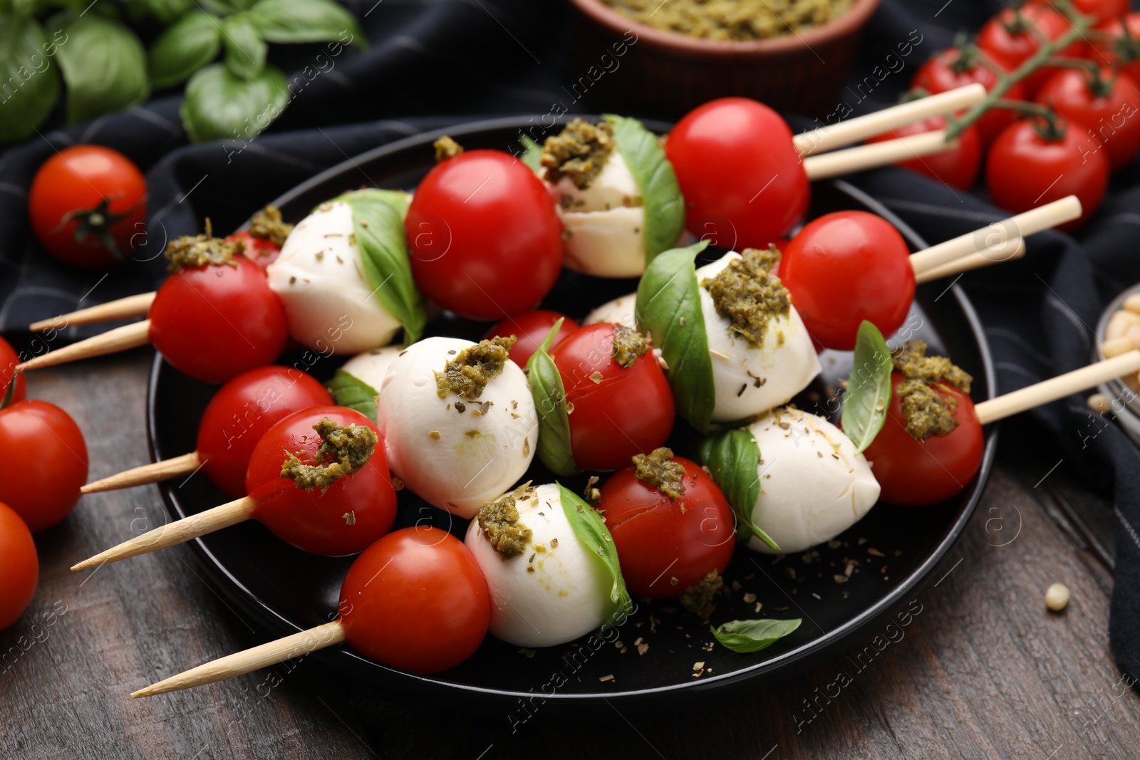 Photo of Caprese skewers with tomatoes, mozzarella balls, basil and pesto sauce on wooden table, closeup