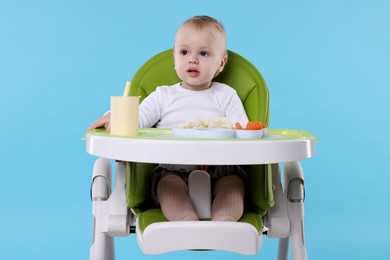 Cute little baby with healthy food in high chair on light blue background