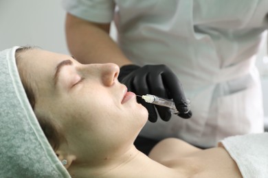 Cosmetologist giving lips injection to patient indoors, closeup. Cosmetic surgery