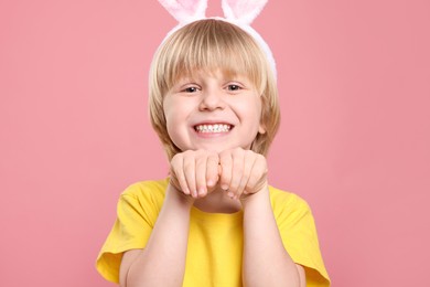 Photo of Happy boy wearing bunny ears headband on pink background. Easter celebration