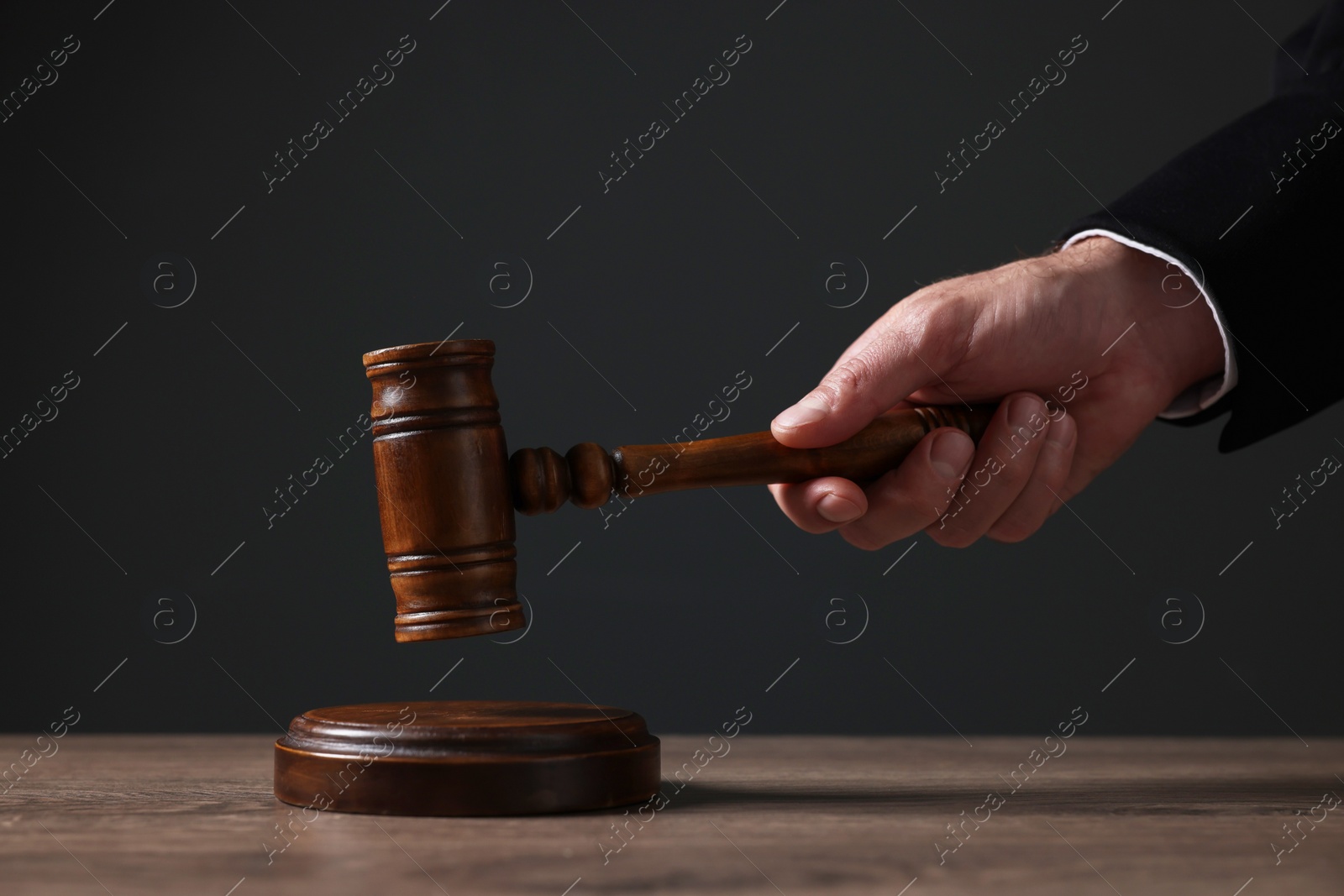 Photo of Judge with gavel at wooden table against black background, closeup