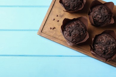 Tasty chocolate muffins on light blue wooden table, top view. Space for text