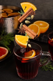 Image of Cut orange and different spices falling into glass cup of mulled wine on table