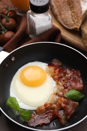Photo of Fried egg, bacon and basil in frying pan on table
