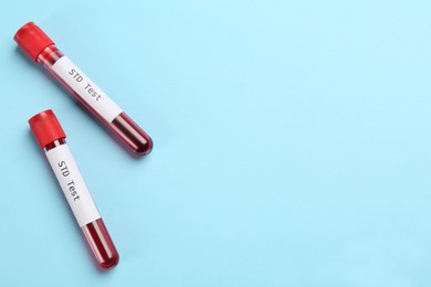 Photo of Tubes with blood samples and labels STD Test on light blue background, flat lay. Space for text