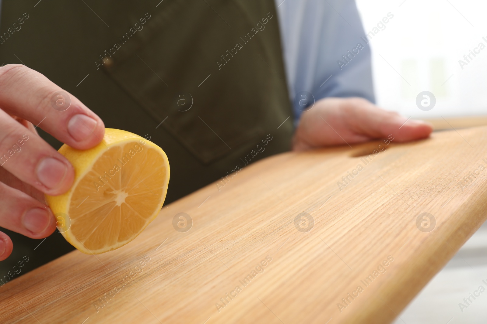 Photo of Man rubbing wooden cutting board with lemon on light background, closeup