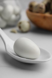 Photo of One boiled quail egg in spoon on white table, closeup