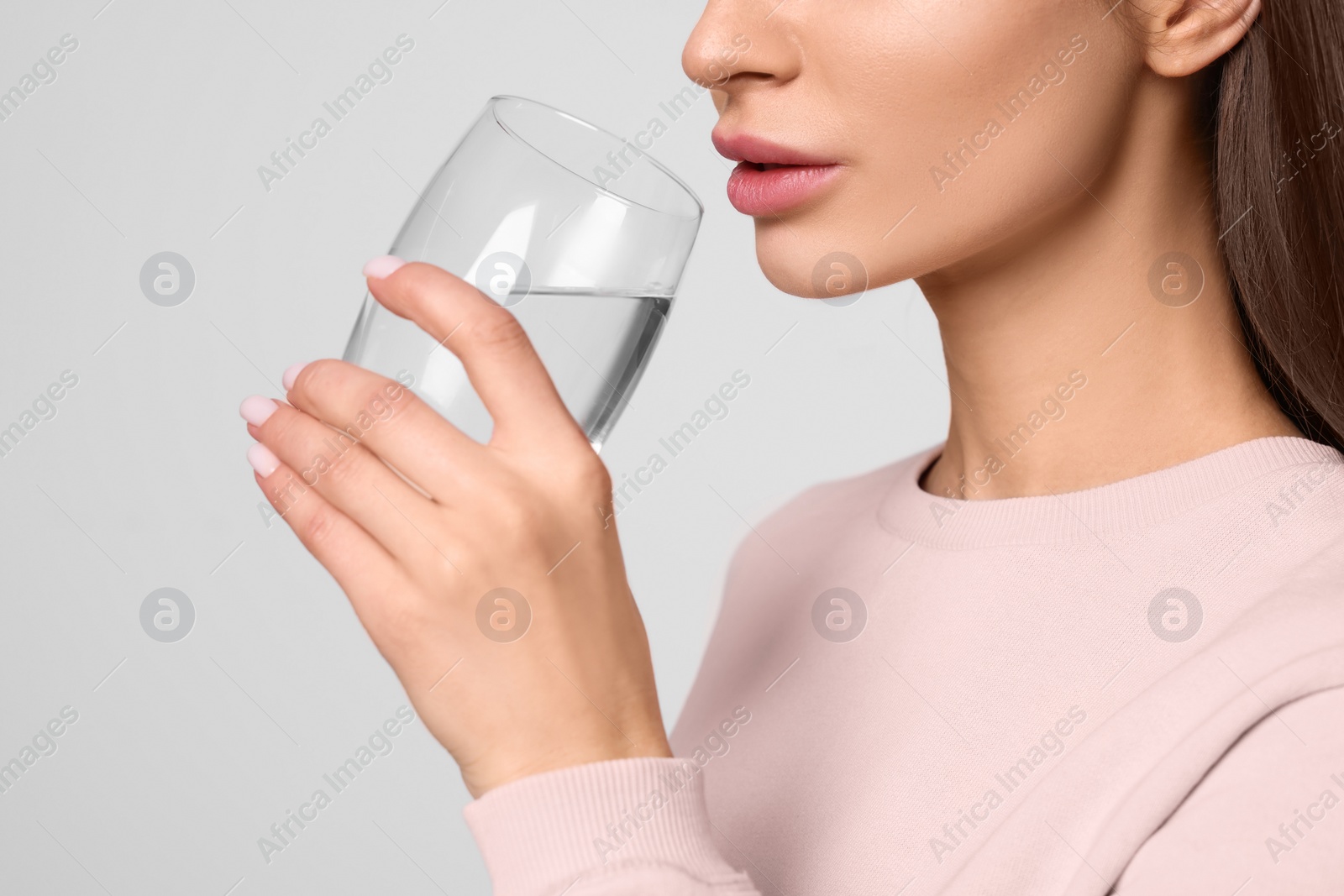 Photo of Healthy habit. Woman drinking fresh water from glass on light grey background, closeup